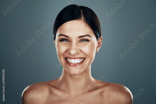 Beautiful young woman looking at camera and smiling while standing against grey background