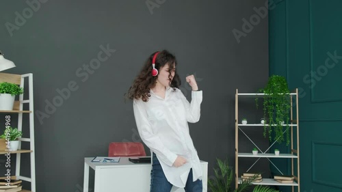 Beautiful curly haired girl listening to a music. Businesswoman singing and dancing at the home office, taking a break from work and having fun.