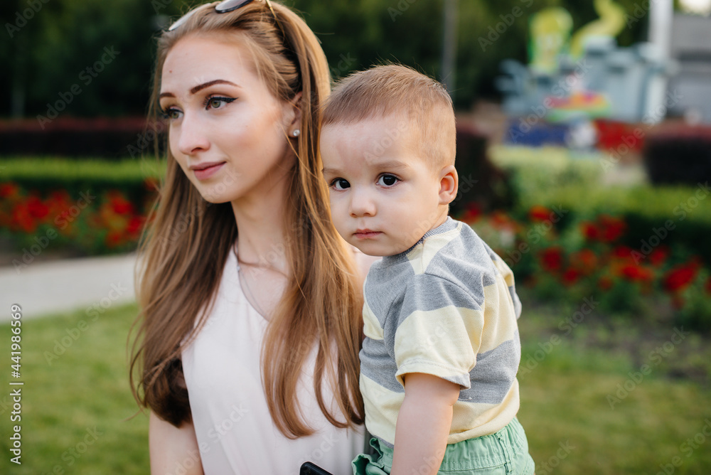 A young beautiful mother plays and hugs her little son during the sunset in the park. Happy family walk in the park. A young beautiful mother plays and hugs her little son during the sunset in the park. Happy family walk in the park.