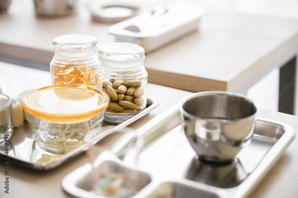 Bottle of supplement capsules is placed in a tray on a table against a blurred background. Health care concept. Bottle of supplement capsules is placed in a tray on a table against a blurred background. Health care concept.