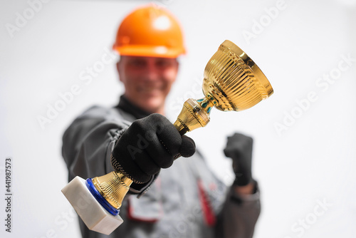 Builder contractor in the hardhat with a golden award cup in hand isolated on the white background. Best worker of the year concept. photo