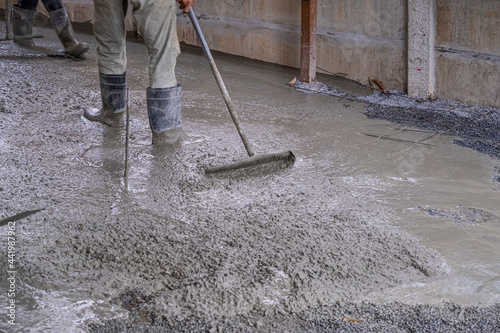worker man dirty working wet cement on floor by use trowel with long Tools spreading poured concrete for strong street after dry.