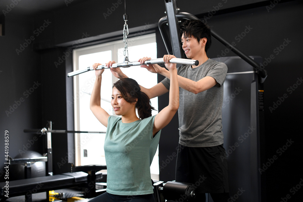 ラットプルダウンをするアジア人女性と補助をする男性トレーナー Stock Photo Adobe Stock