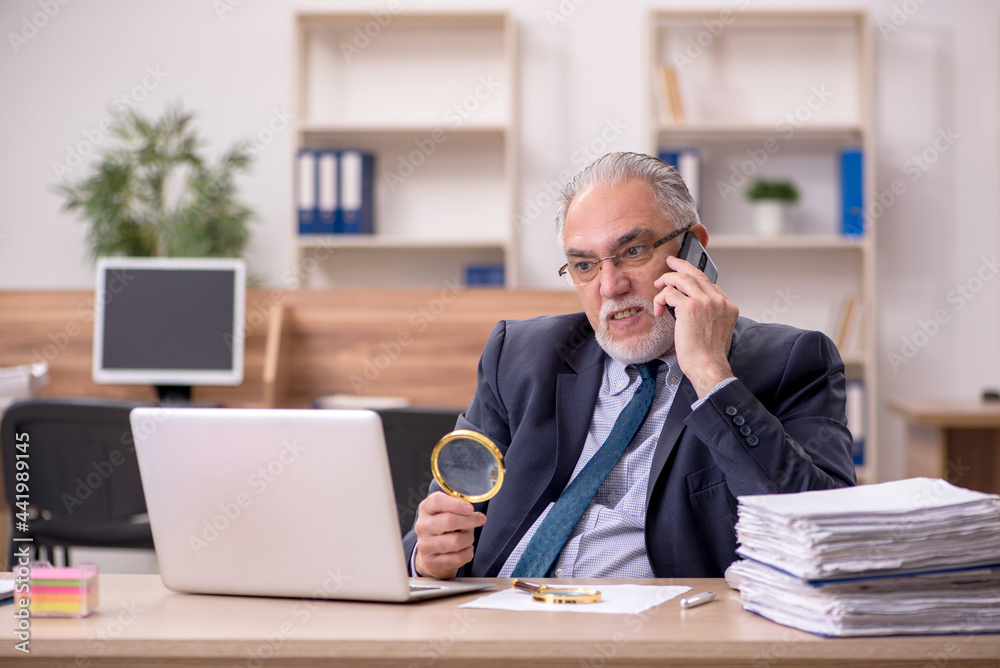 Old male employee auditor holding loupe at workplace Old male employee auditor holding loupe at workplace
