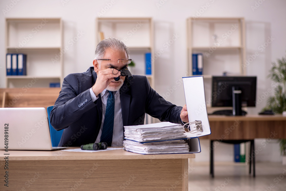 Old male employee auditor holding binoculars at workplace Old male employee auditor holding binoculars at workplace