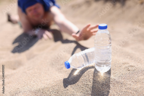 Man stretching his hands with plastic bottle of water in desert closeup