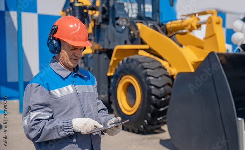 Industrial mechanic uses tablet test online status of bulldozer at construction site. Concept optimization of work of business processes in building