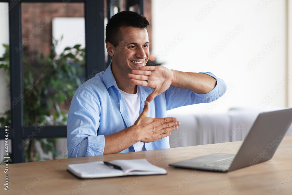 Happy smiling deaf young caucasian man uses sign language while video call using laptop while sitting at home, virtual communication concept Happy smiling deaf young caucasian man uses sign language while video call using laptop while sitting at home, virtual communication concept