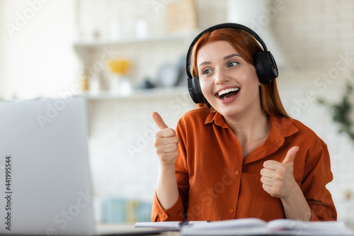 E-learning, online communication. Joyful girl student in headphone uses laptop for online education, studying remotely at home, smiling