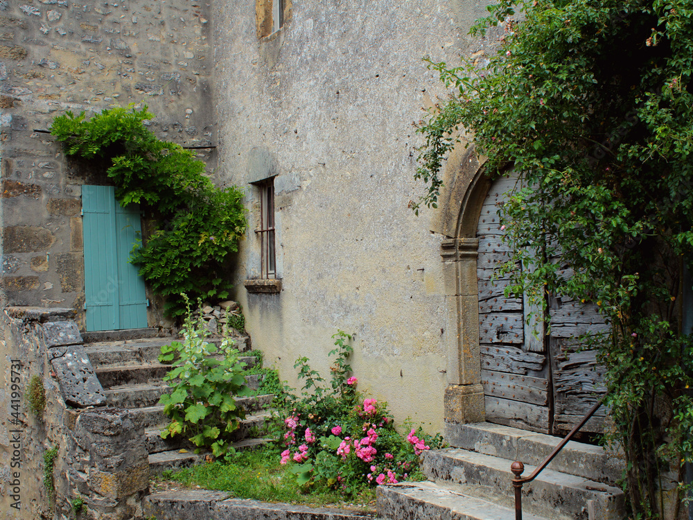 Fototapeta premium Fresh green plants and flowers around rustic old doors of charming country-style grey stone medieval houses in Vezelay village, Burgundy, France, a popular European tourist destination.