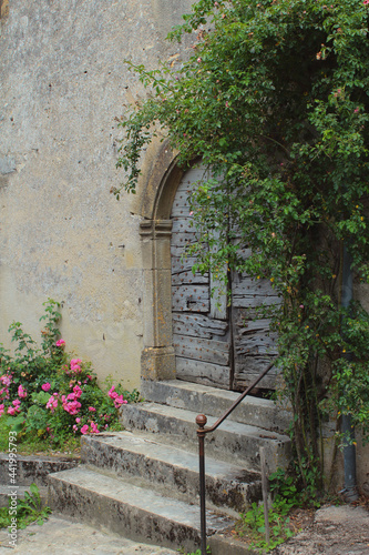 Fototapeta Naklejka Na Ścianę i Meble -  Fresh green plants and flowers around rustic old doors of charming country-style grey stone medieval houses in Vezelay village, Burgundy, France, a popular European tourist destination.