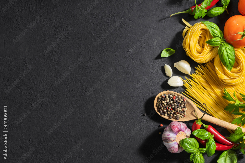 Ingredients for cooking italian food, pasta, tomatoes, pepper, garlic and parsley on dark background with copy space, top view