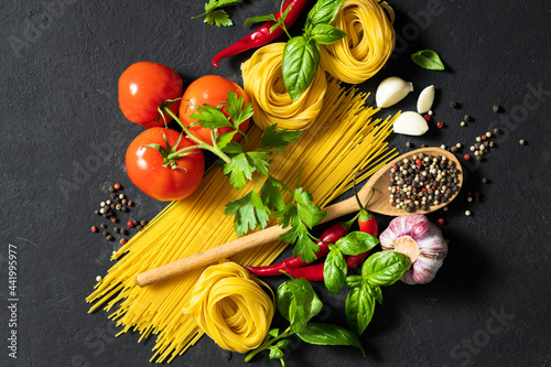 Italian food cuisine and ingredients. Spaghetti and tagliatelle with tomatoes  pepper  garlic and parsley on dark background  top view