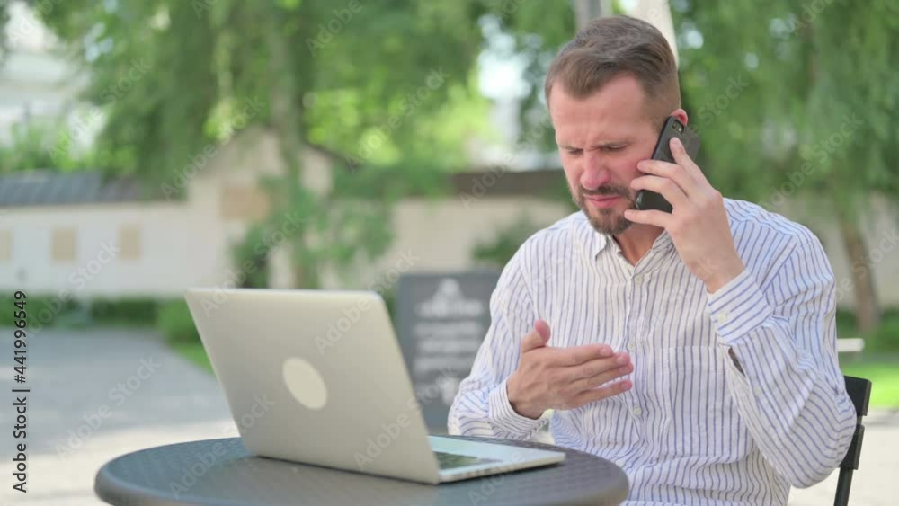 Angry Middle Aged Man Talking on Smartphone in Outdoor Cafe Angry Middle Aged Man Talking on Smartphone in Outdoor Cafe