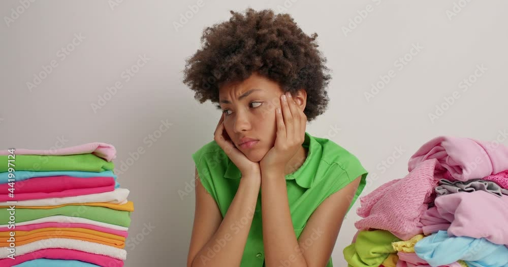 Displeased tired ethnic housewife busy folding laundry leans at table ...