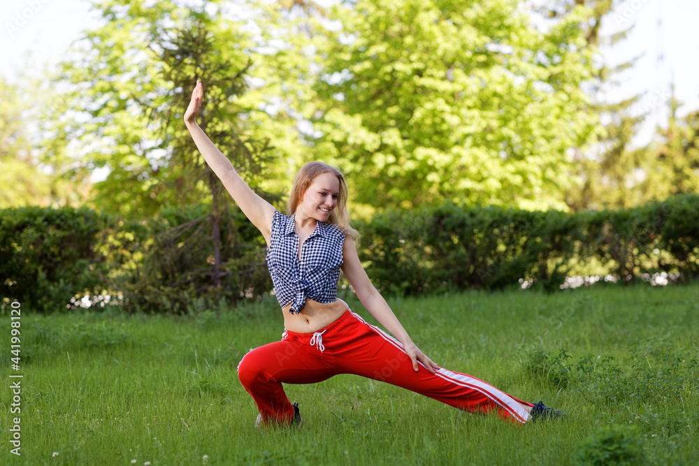 Young girl doing warm-up and doing stretch in the park on a sunny summer day. Shallow focus. Young girl doing warm-up and doing stretch in the park on a sunny summer day. Shallow focus.
