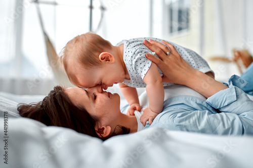 Loving mom carying of her newborn baby at home.Mom and baby boy playing in sunny bedroom. Parent and little kid relaxing at home. Family having fun together. Childcare, maternity concept. photo