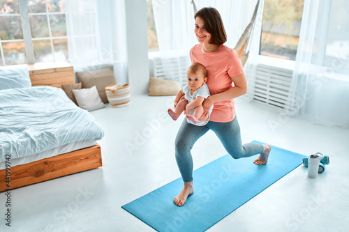 A sports mother is engaged with the child in fitness and yoga at home. The concept of sports, motherhood and an active lifestyle. Young woman in sports training with her child. © Valerii Apetroaiei