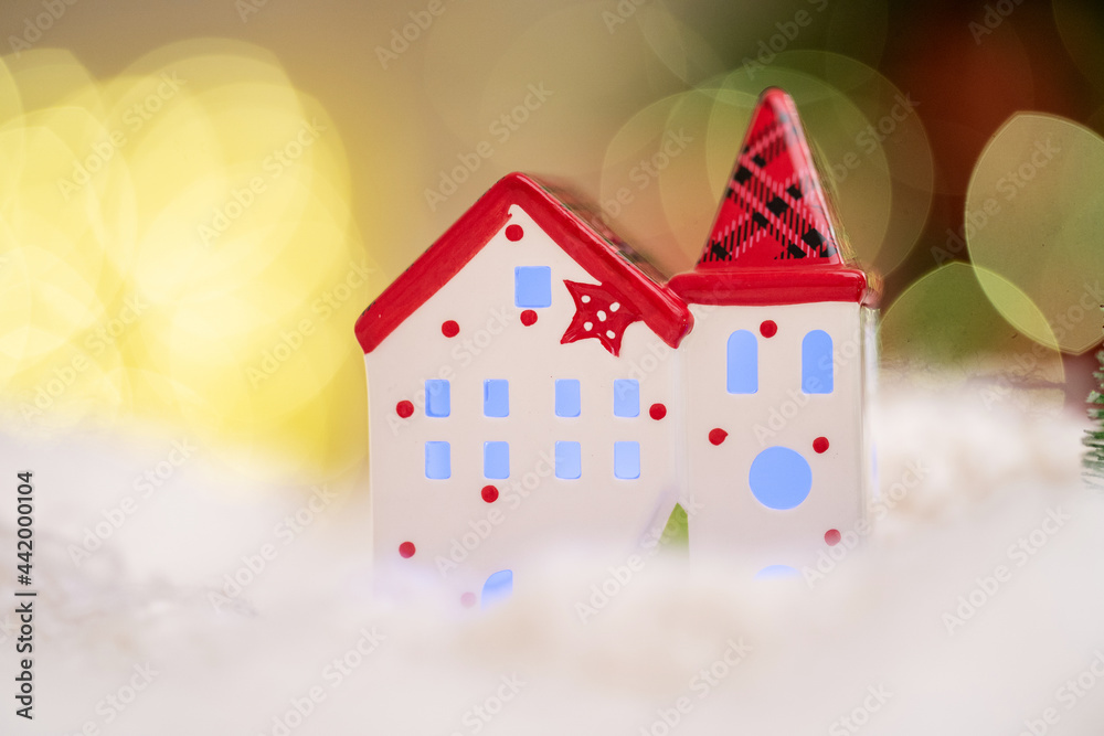 beautiful festive background with decorative ceramic candle holder in shape house. white house on blurry, muted background with golden bokeh and garland.. Christmas candle holder, New Year 2022