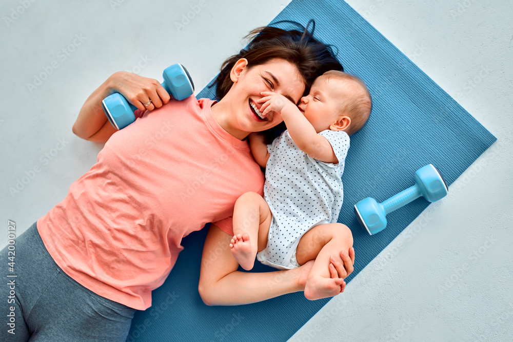 Fototapeta A sports mother is engaged with the child in fitness and yoga at home. The concept of sports, motherhood and an active lifestyle. Young woman in sports training with her child.