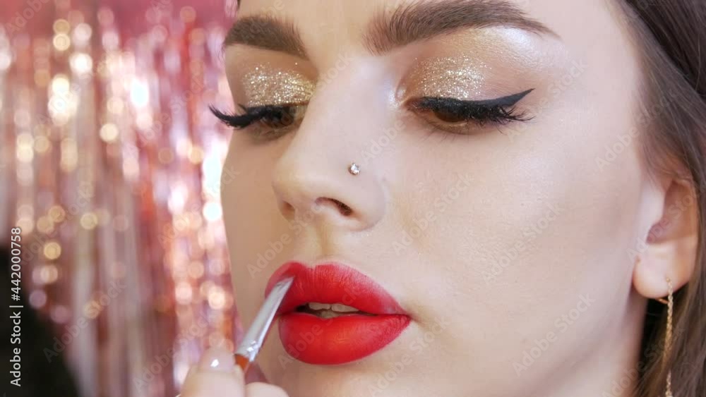 Bright lip makeup, big beautiful lips are painted with red lipstick with a special brush in a beauty salon. Professional make-up. Makeup with black arrow