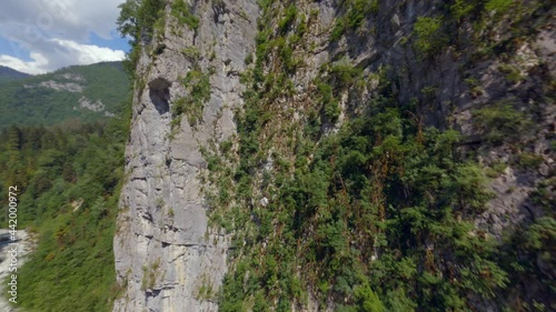 Extreme fast fpv flight over beautiful nature landscape with high mountain canyon covered by dense green trees. Aerial shot natural rapid movement rock river with speed foamy water at hilly terrain photo