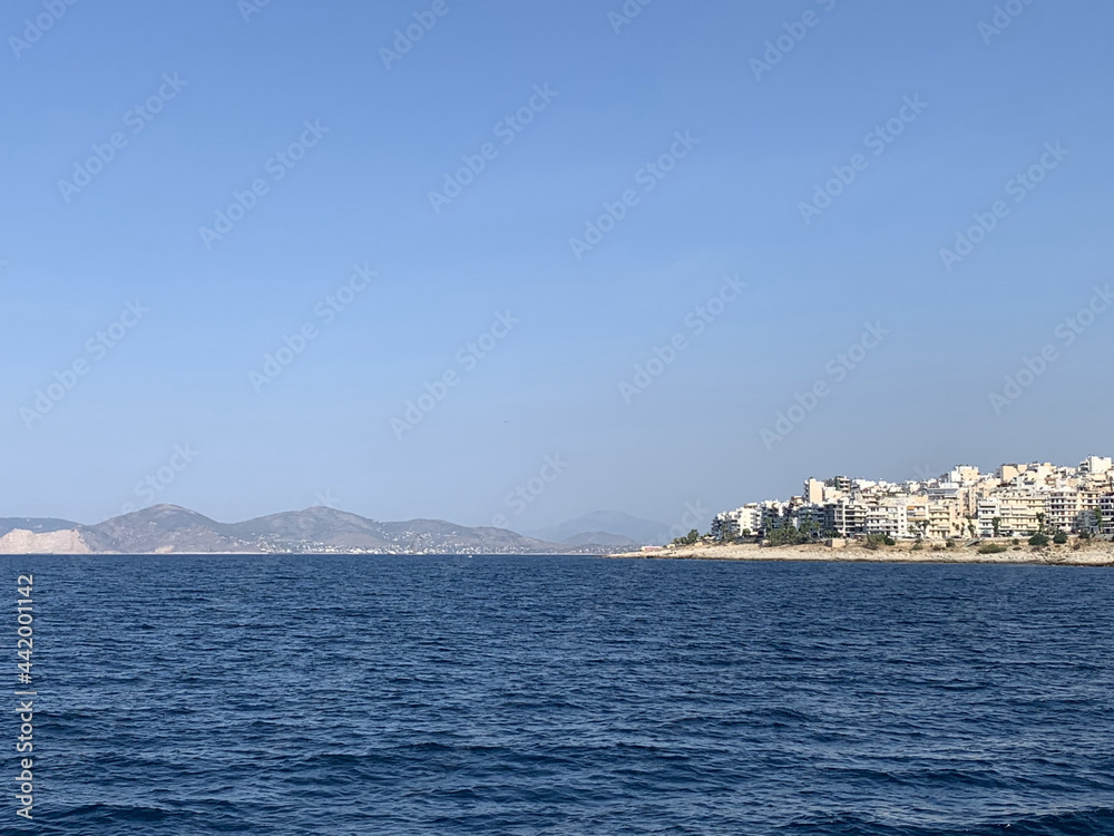 Greek city and mountains in the distance from ocean with blue skies