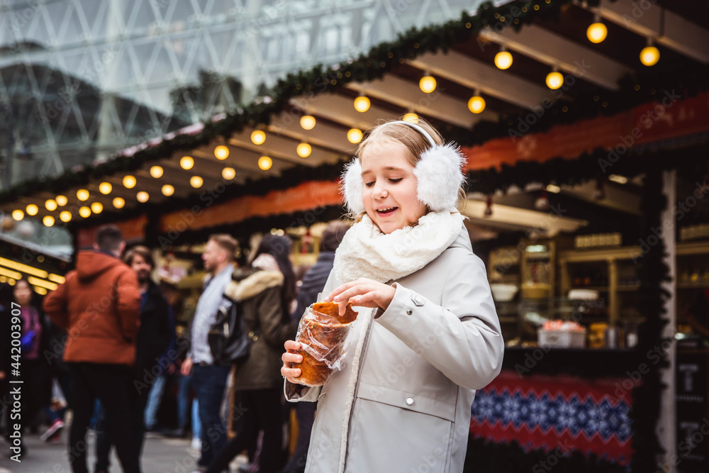 A cute little girl eats a traditional Hungarian sweet pastry called Kurtoskalacs in Budapest on the street market at wintertime