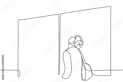 man stands in front of closed doors with a backpack on his back, his face pointing up - one line drawing vector. concept of impatient passenger waiting for boarding start