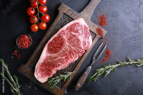 Raw meat steak. Japanese marble wagyu meat on a dark wooden board with spices, rosemary and fresh cherry tomatoes. Background image, copy space. Top view, flatlay photo
