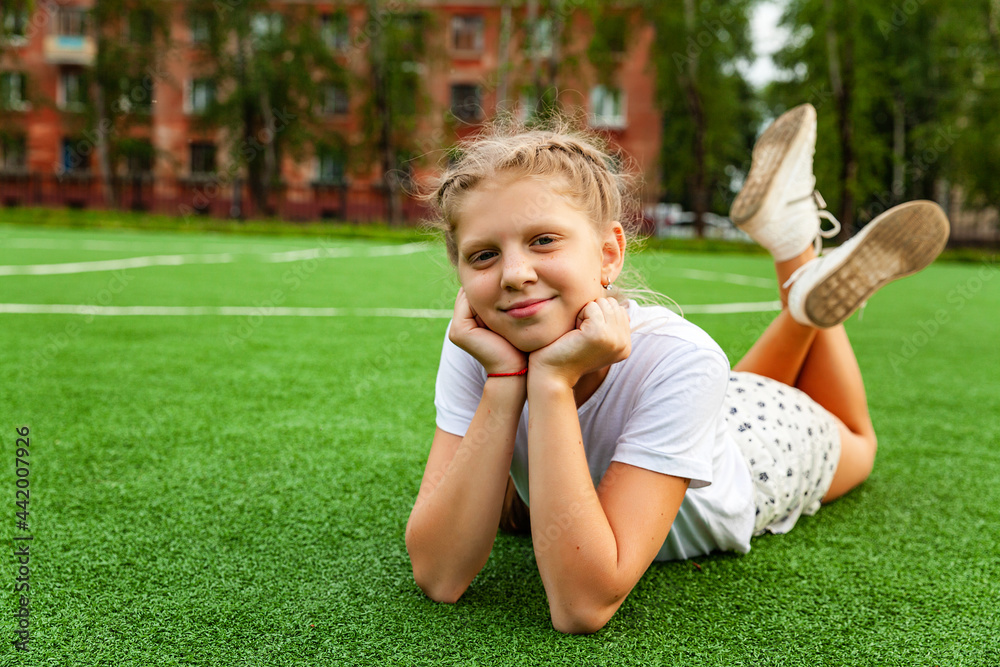 A happy girl lies on the grass on the playground. Daytime, stadium, open air A happy girl lies on the grass on the playground. Daytime, stadium, open air