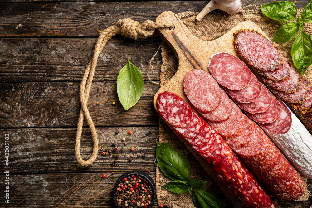 Set of different types of sausages, salami and smoked meat with basil and spices on wooden background. Top view.