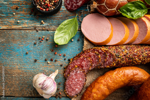 Set of different types of sausages, salami and smoked meat with basil and spices on wooden background. Top view.