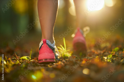 Close up of female legs in sport sneakers jogging at city park during morning time. Concept of people, fitness and workout.