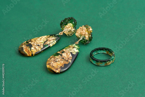 Close up shot of set of a ring and dangle earrings made of epoxy resin with golden foil inside isolated over green background photo