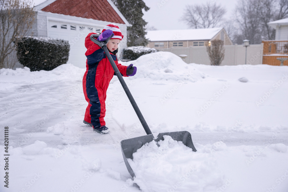 Toddler helping to shovel snow in the driveway of their house