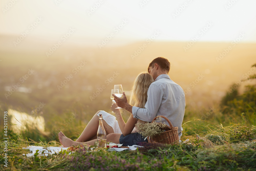 A loving couple is enjoying a summer picnic, beautiful landscape and sunset with wine.