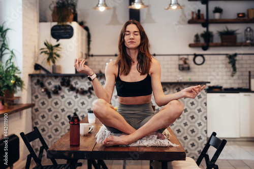 Sporty woman sits on a table with her eyes closed and meditates.