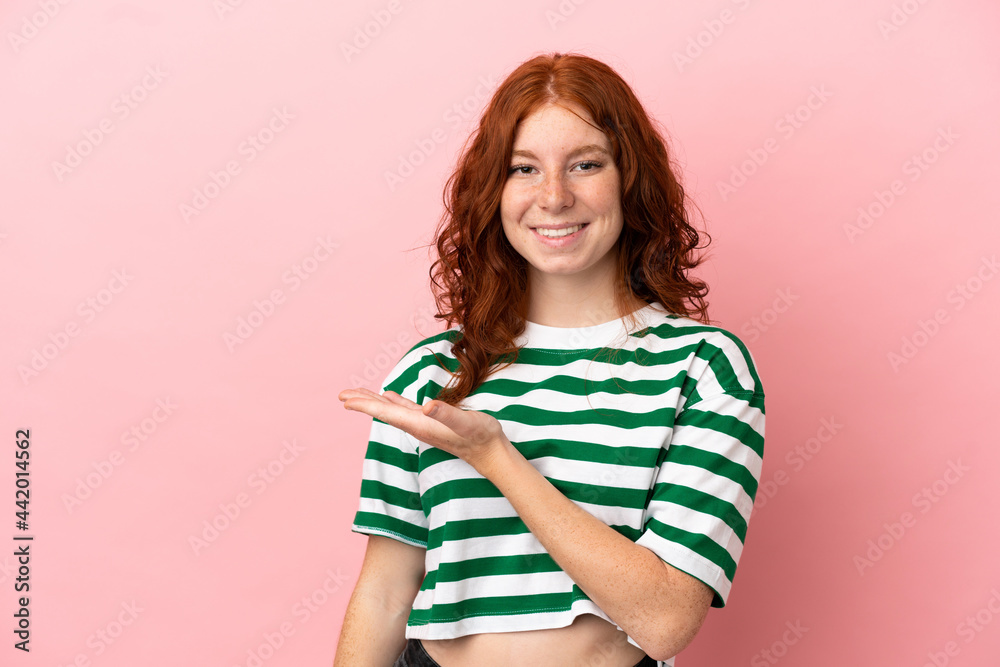 Teenager redhead girl over isolated pink background presenting an idea while looking smiling towards Teenager redhead girl over isolated pink background presenting an idea while looking smiling towards
