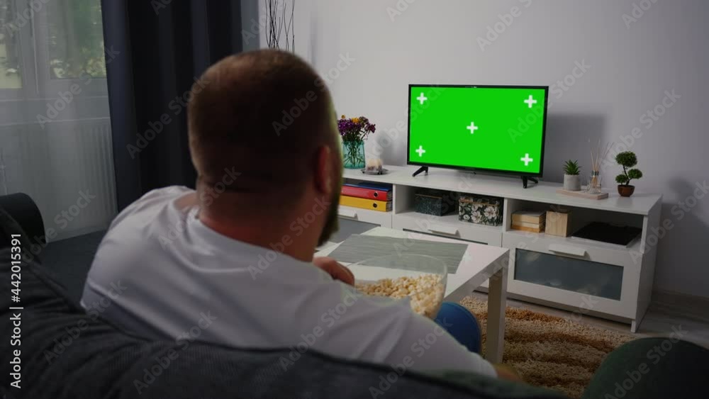 Man Watching Green Chroma Key Tv Screen and Changing Channels with Remote Control several times. Male sitting on the couch in the living room in the evening Man Watching Green Chroma Key Tv Screen and Changing Channels with Remote Control several times. Male sitting on the couch in the living room in the evening