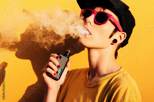 Modern woman vaping against yellow wall photo