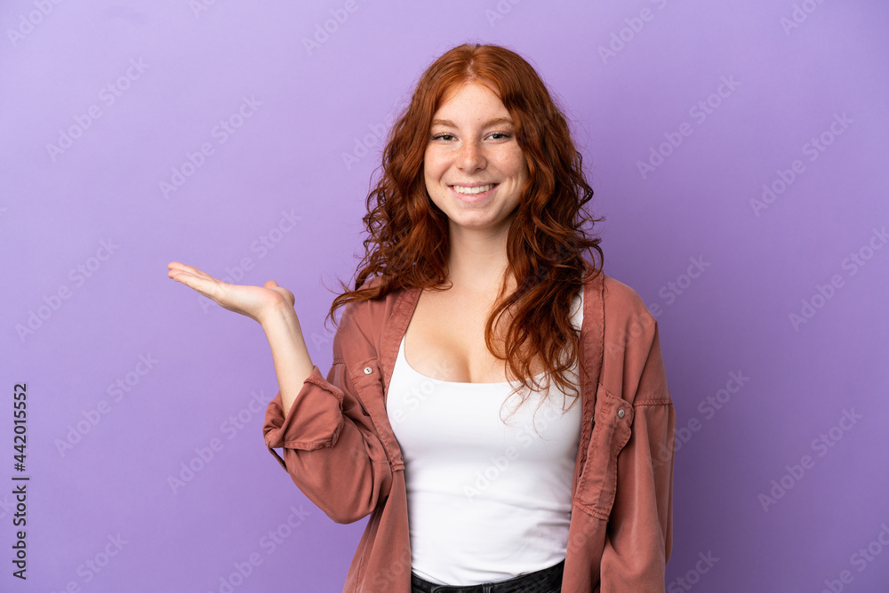 Teenager redhead girl over isolated purple background holding copyspace imaginary on the palm to insert an ad Teenager redhead girl over isolated purple background holding copyspace imaginary on the palm to insert an ad