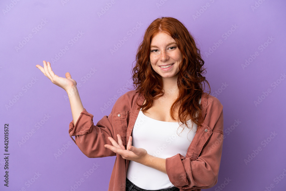 Teenager redhead girl over isolated purple background extending hands to the side for inviting to come Teenager redhead girl over isolated purple background extending hands to the side for inviting to come