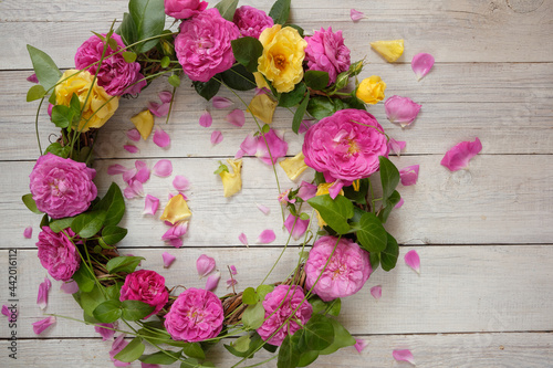 A wreath of roses and green leaves on a white wooden background. Flowers flat lay, top view. Background with copy space. Beautiful background for advertising cosmetics.