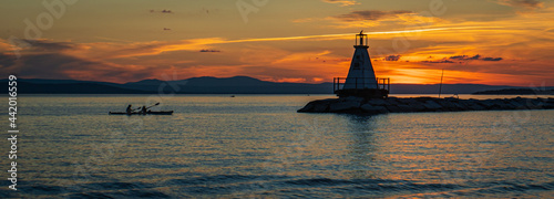 banner photo of kayakers approaching the Lake Champlain breakwater's lighthouse with a sea bird perched on the top at sunset 
