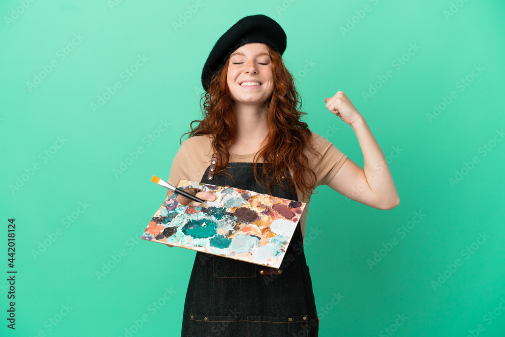 Teenager redhead artist holding a palette isolated on green background doing strong gesture Teenager redhead artist holding a palette isolated on green background doing strong gesture