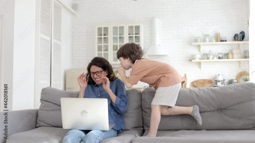 Bored hyperactive kid jumping and making noise at frustrated young mother trying to concentrate on freelance work in laptop on lockdown adn school quarantine. Mom parent tired of srubborn son at home