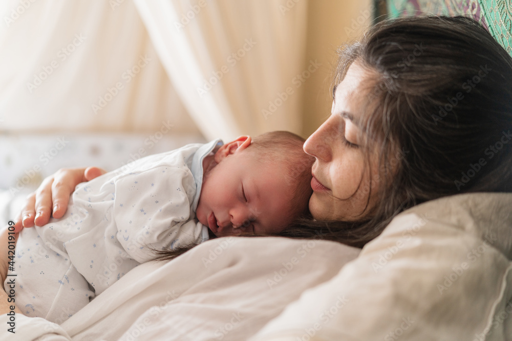 Mother cuddling sleeping newborn baby on bed Mother cuddling sleeping newborn baby on bed