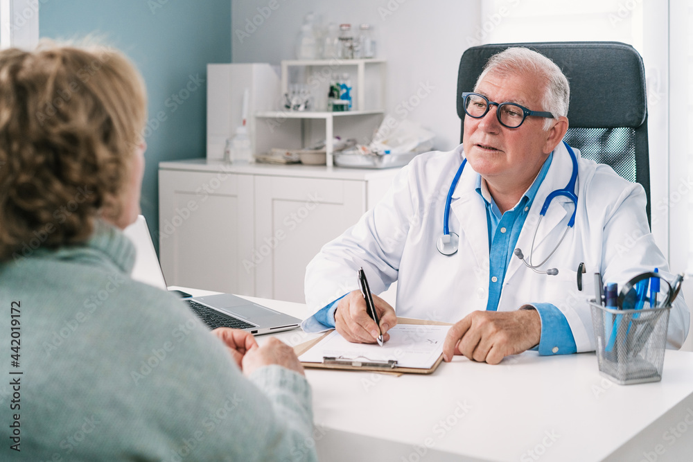 Senior physician writing on document during consultation with anonymous patient Senior physician writing on document during consultation with anonymous patient