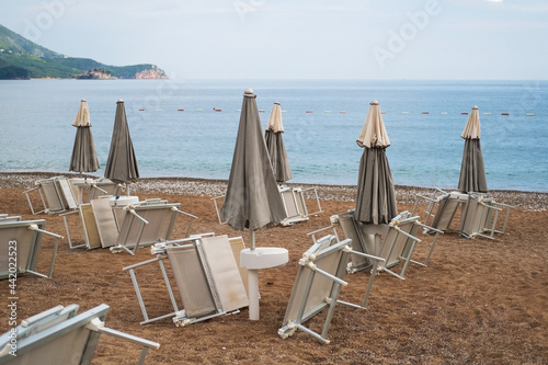 inverted sun loungers under umbrellason the pebble beach by the sea © ukrolenochka